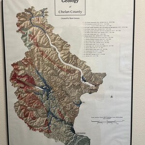 May include: A framed geological map of Chelan County, Washington, with a detailed topographic representation. The map features a color-coded geological key and scale, with text that reads "Geology of Chelan County" and "Created by Ryan Lennon."