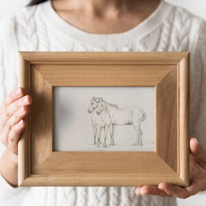 May include: A wooden frame with a black and white pencil drawing of two horses standing side by side.