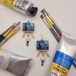 May include: A pair of gold earrings with a miniature canvas painting of Van Gogh's Starry Night. Each earring has a pearl and a blue crystal dangle.