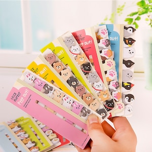 May include: A set of colourful sticky notes with cute animal designs. Each note has a different animal face peeking out from the top. The notes are labelled "Stick Marker Peep Out!" and "Composure creates time to the full."