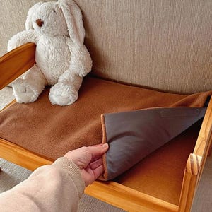 May include: A miniature wooden pet bed with a brown fleece blanket and a white stuffed bunny. The bed has a simple design with a rectangular frame, ideal for small pets to rest on.