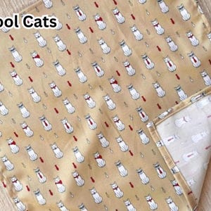May include: A tan fabric with a repeating pattern of white cats wearing ties and bowties, with the text "Cool Cats" in the upper left corner. The cats are interspersed with red teardrop shapes.