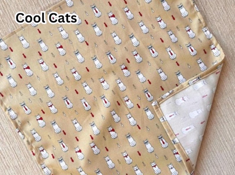 May include: A tan fabric with a repeating pattern of white cats wearing ties and bowties, with the text "Cool Cats" in the upper left corner. The cats are interspersed with red teardrop shapes.