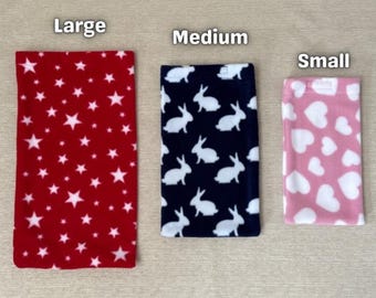 Peut inclure: Trois pochettes doublées de polaire de différentes tailles, étiquetées "Large", "Moyen" et "Petit". La grande pochette est rouge avec des étoiles blanches, la pochette moyenne est bleu marine avec des lapins blancs et la petite pochette est rose avec des cœurs blancs.