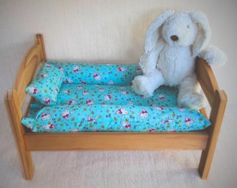 May include: A wooden doll bed with a blue and white bunny print bedding set. A white plush bunny sits on the bed.