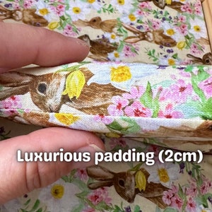Op de afbeelding: Close-up van een stof met een bloemenpatroon met roze bloemen, groene bladeren en bruine konijnen. De stof is gevouwen om een ​​2 cm dikke vulling te laten zien.