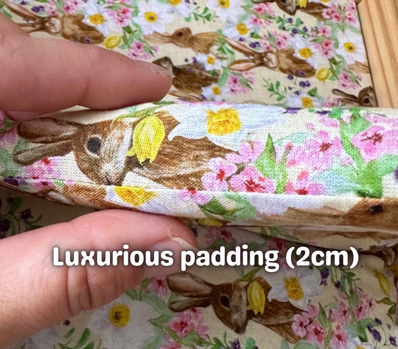 Op de afbeelding: Close-up van een stof met een bloemenpatroon met roze bloemen, groene bladeren en bruine konijnen. De stof is gevouwen om een ​​2 cm dikke vulling te laten zien.
