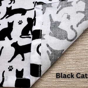 May include: White fabric with a repeating pattern of black cat silhouettes in various poses, including paw prints and small mouse illustrations. The words "Black Cats" are printed in black on the fabric.