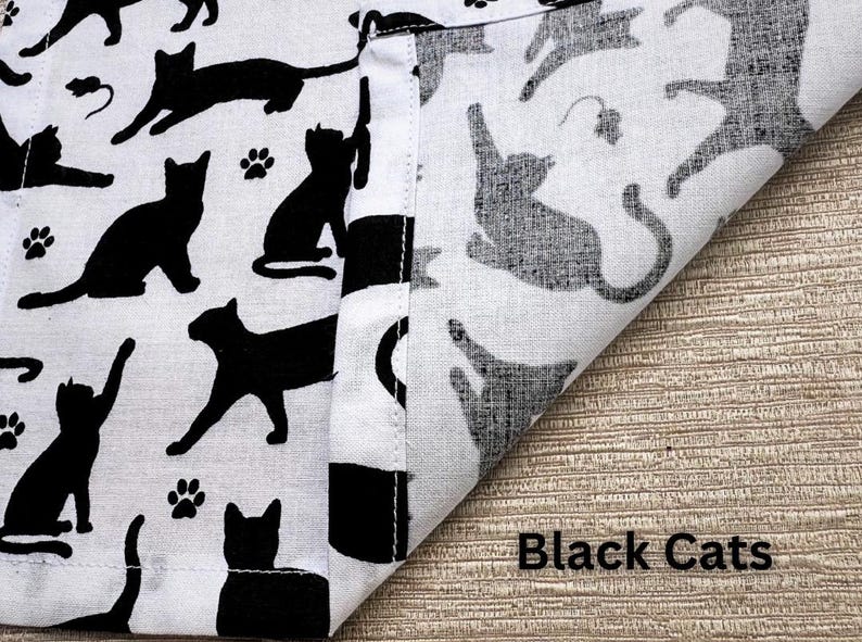 May include: White fabric with a repeating pattern of black cat silhouettes in various poses, including paw prints and small mouse illustrations. The words "Black Cats" are printed in black on the fabric.