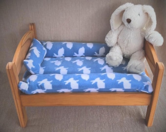 May include: A wooden doll bed with a blue and white patterned fleece mattress and pillow. A white plush bunny sits on the bed.