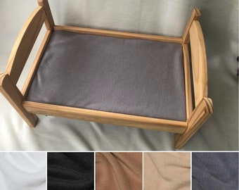 May include: A wooden doll's bed with a grey fleece mattress. The bed is shown with different colour fleece mattress options: white, black, brown, beige, and grey.