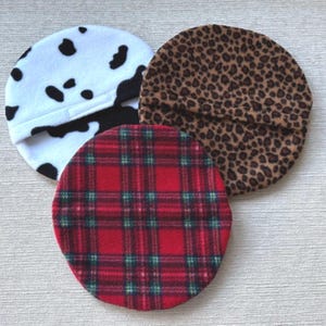 May include: Three fleece berets in different patterns: cow print, leopard print and red tartan.