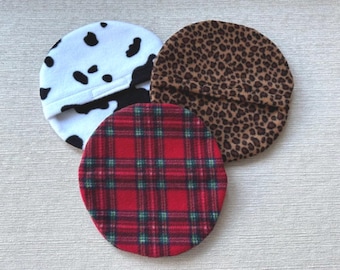 May include: Three circular fabric covers featuring distinct patterns: one with a white and black cow print, one with a brown and black leopard print, and one with a red, green, and black plaid design. Each cover has a visible horizontal seam.