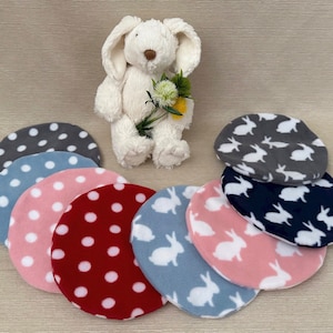 May include: A set of eight fleece fabric circles with different patterns.  The circles are in shades of grey, blue, pink, and red.  Some circles have a white polka dot pattern, while others have a white bunny silhouette pattern.