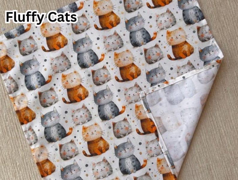 May include: White fabric with a repeating pattern of cartoon cats in orange, gray, and white. The cats are in various poses, with small dots scattered around them. The words "Fluffy Cats" are in the upper left corner.