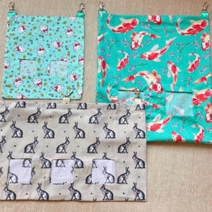 May include: Three rectangular fabric hanging pouches with metal clips. One small pouch features a light blue background with white cat faces. A larger pouch has a teal background with red and white koi fish. A wide pouch features a beige background with black rabbit silhouettes.