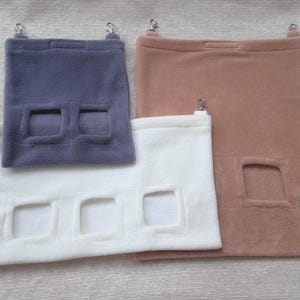 May include: Three hanging pouches for small pets, made of soft, plush fabric. The pouches have different colored fabric: gray, white, and brown. Each pouch has one or more openings for the pet to enter and exit.