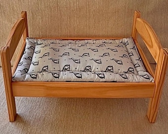 May include: A small wooden bed frame with a light brown finish and arched headboard and footboard. The bed includes a rectangular mattress pad featuring a light gray fabric cover with a repeating pattern of dark gray rabbits and small dots.