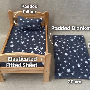 K&ouml;nnte beinhalten: Ein Holz-Puppenbett mit einem grauen Spannbettlaken mit wei&szlig;en Sternen, einem grauen, gepolsterten Kissen mit wei&szlig;en Sternen und einer grauen, gepolsterten Decke mit wei&szlig;en Sternen. Die Decke misst 30 cm x 48 cm.