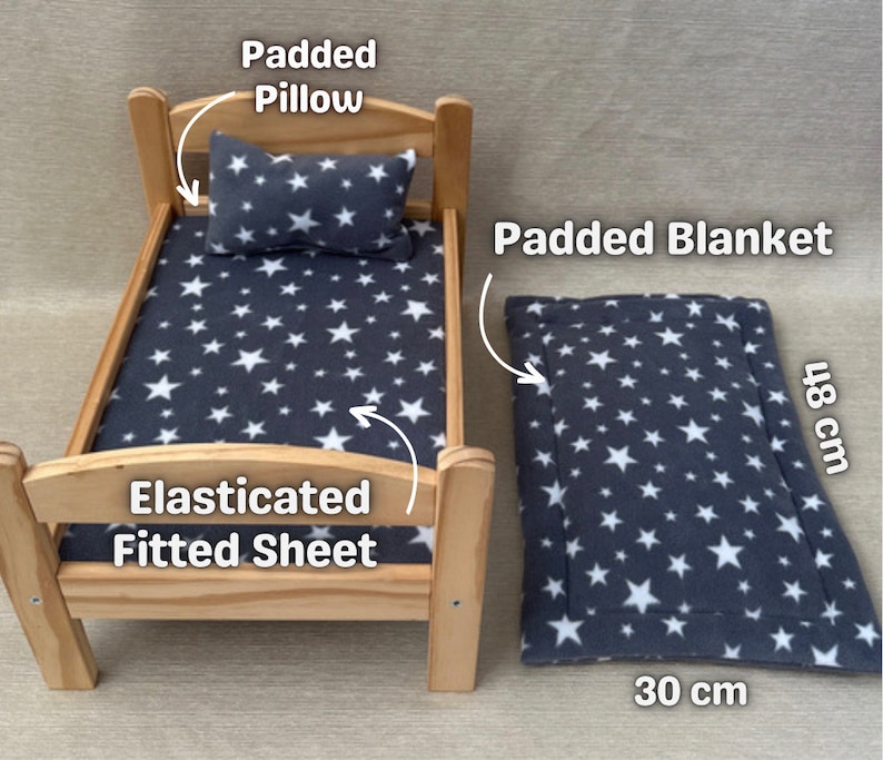 K&ouml;nnte beinhalten: Ein Holz-Puppenbett mit einem grauen Spannbettlaken mit wei&szlig;en Sternen, einem grauen, gepolsterten Kissen mit wei&szlig;en Sternen und einer grauen, gepolsterten Decke mit wei&szlig;en Sternen. Die Decke misst 30 cm x 48 cm.