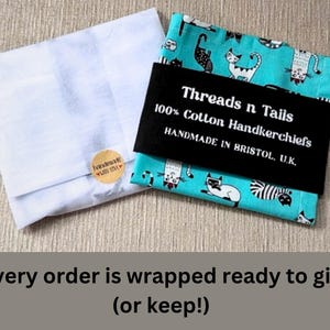 May include: Two handkerchiefs, one white and one teal with a cat pattern, are shown. The teal handkerchief is wrapped with a black band that reads "Threads n Tails 100% Cotton Handkerchiefs HANDMADE IN BRISTOL, U.K."
