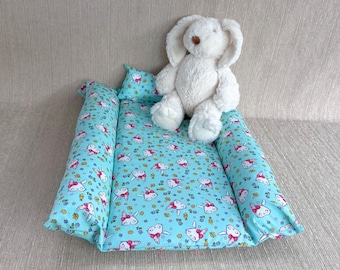 May include: A light blue baby nest with a white bunny pattern and a white plush bunny toy. The nest is made of soft fabric and has a raised edge to keep the baby safe and comfortable.