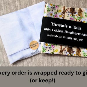 May include: A white tissue paper wrapping with a brown label that says "handmade with love". The tissue paper is wrapped around a handkerchief with a floral pattern and a black label that says "Threads n Tails 100% Cotton Handkerchiefs HANDMADE IN BRISTOL, U.K."