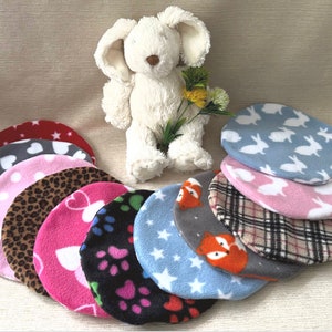 Puede incluir: Una colección de diez camas redondas para mascotas de forro polar en varios colores y patrones, incluyendo rojo con estrellas blancas, gris con corazones blancos, rosa con corazones blancos, marrón con estampado de leopardo, rosa con corazones blancos, negro con huellas de patas, azul con estrellas blancas, gris con zorros naranjas, beige a cuadros y rosa con conejos blancos.