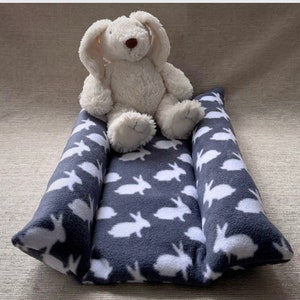 May include: A gray and white fleece pet bed with a white bunny pattern. A white plush bunny toy is sitting on the bed.