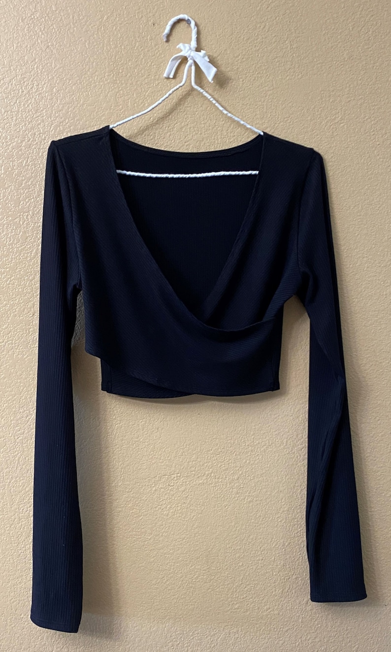 K&ouml;nnte beinhalten: Ein schwarzes, lang&auml;rmliges Crop-Top mit V-Ausschnitt und Wickeldetail.
