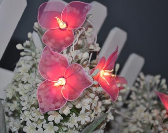 May include: A string of fairy lights with pink flower-shaped bulbs. The lights are strung through a bouquet of white flowers.