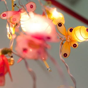 May include: A string of fairy lights featuring butterfly and bee shapes. The lights are made from delicate fabric and have a warm glow.