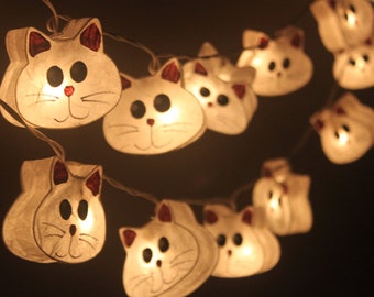 May include: A string of white cat-shaped paper lanterns with small light bulbs inside. The lanterns are strung together with a clear wire and are lit up, creating a warm glow.