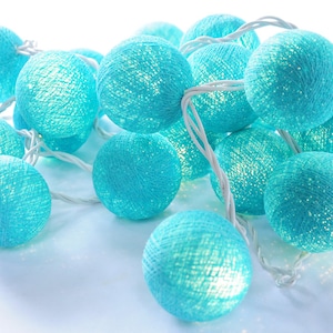 May include: A string of teal blue cotton ball lights with white wire. The lights are strung together in a cluster and are lit up.