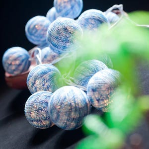 May include: A string of blue and white cotton ball lights. The lights are strung together with a clear wire and are illuminated with warm white LED lights.