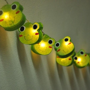 May include: A string of green frog-shaped lights with a yellow glow. The lights are strung together with a clear wire.