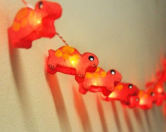 May include: A string of red paper turtle-shaped lights with a warm white glow. The lights are strung together with clear wire.