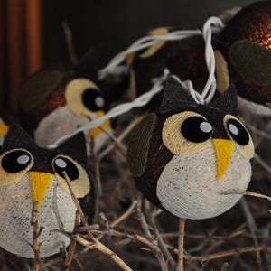 May include: A string of owl-shaped lights with a brown and white patterned design. The lights are strung on a wire and are lit up. The owls are all facing the same direction.