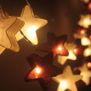May include: A string of white and burgundy star-shaped paper lanterns with warm white lights. The lights are strung together with clear wire.