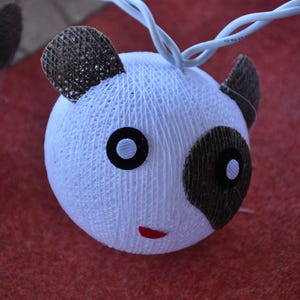 May include: A string of white cotton ball lights shaped like pandas. Each panda has black eyes and ears, and a black and white face.