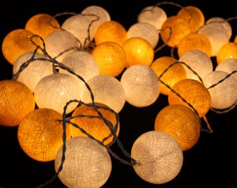 Puede incluir: Una cadena de luces de bola de algodón con una mezcla de bombillas blancas cálidas y amarillas. Las luces están enhebradas con un cable delgado.
