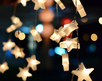May include: A string of white star-shaped lights hanging from a ceiling. The lights are illuminated and create a warm glow.