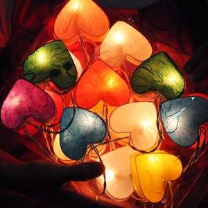 May include: A string of heart-shaped paper lanterns with different colors and patterns, including red, pink, green, blue, and yellow. The lanterns are lit from within, creating a warm and inviting glow.