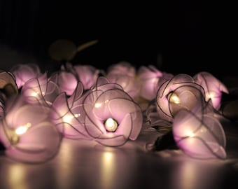 May include: A string of fairy lights with delicate, purple flower-shaped shades. Each light has a warm white LED bulb inside, creating a soft glow.