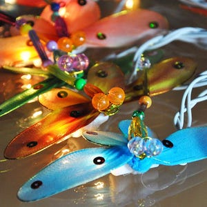 Puede incluir: Una cadena de luces de hadas con luces de colores en forma de mariposa y cuentas. Las luces están enhebradas en un cable transparente y tienen un brillo blanco cálido.
