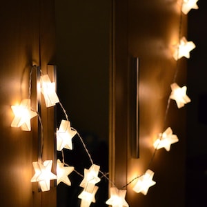 May include: A string of white star-shaped lights with warm white bulbs, hanging on a wooden surface.