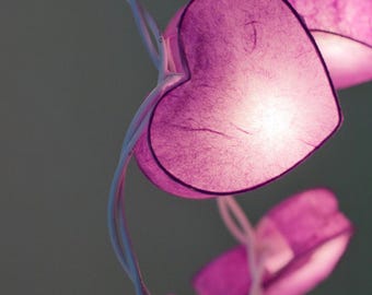 May include: A string of purple heart-shaped paper lights with warm white LED bulbs. The lights are strung on a white wire.