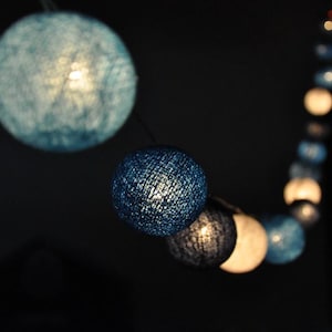 May include: A string of blue and white cotton ball lights. The lights are strung together with a clear wire. The lights are lit and glowing.