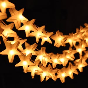 May include: A string of glowing star-shaped lights against a dark background. The warm, yellow lights are arranged in a curved line, creating a festive and inviting atmosphere. Ideal for holiday decorations.
