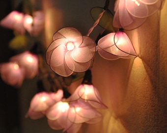 May include: A string of fairy lights with delicate flower-shaped shades in a soft pink hue. The lights are strung together with a clear wire and create a warm, inviting glow.